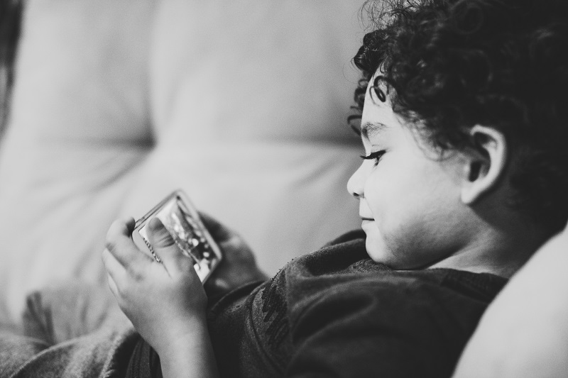 young boy lying on couch watching a video on a smartphone